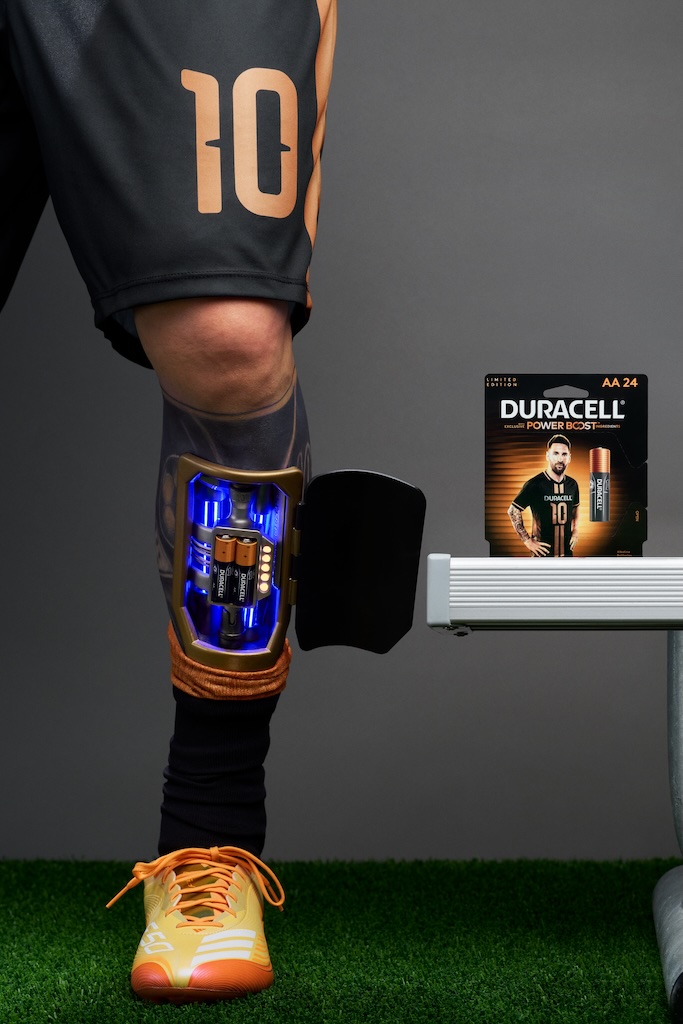 DuracellxMessi_Leg | Muse by Clios Athlete's leg with a blue-lit knee brace, orange cleats, and number 10 shorts; a Duracell Power Boost box sits nearby on a stand.