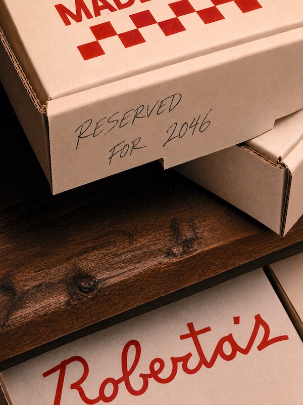 street R | Muse by Clios Pizza boxes on a wooden table with a handwritten note reading “Reserved for 2046” on the front box, and a red Roberta’s logo visible on another box.
