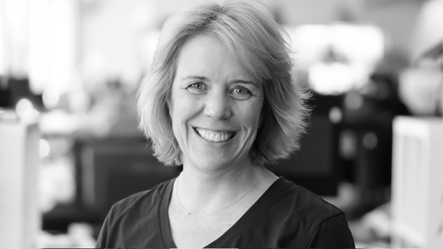 Portrait of a smiling woman with short blonde hair in an office setting, blurred background behind her