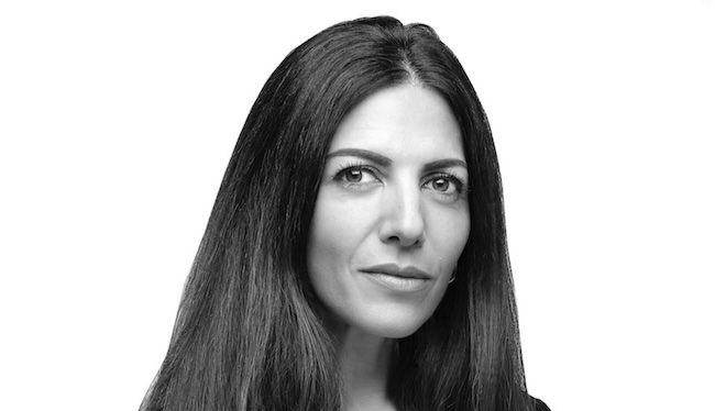 Screenshot | Muse by Clios Portrait of a woman with long dark hair looking at the camera, in a black-and-white photo with a neutral expression.