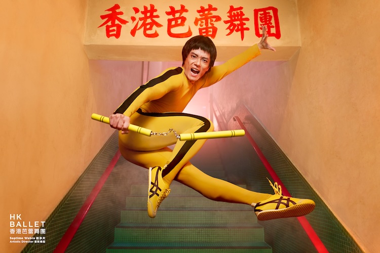 Dancer in a yellow bodysuit leaps mid-air through a stairwell, holding two yellow batons as HK Ballet branding appears in the corner.
