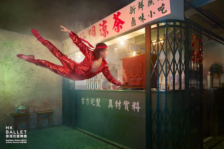 Acrobat in a red shiny jumpsuit flies mid-air in front of a Chinese snack stall at night.