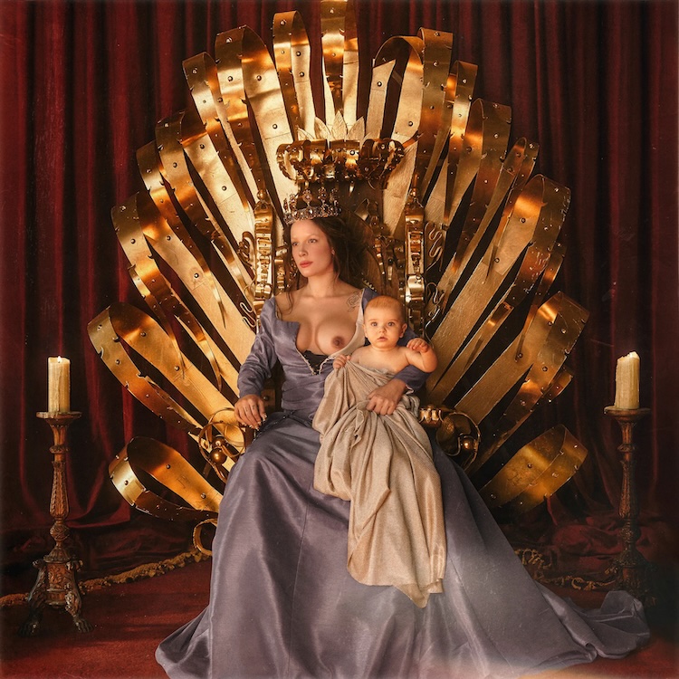 If I Cant Have Love I Want Power Halsey | Muse by Clios A regal woman in a blue-gray gown sits on a large gold throne, holding a baby wrapped in cloth with candles on either side.