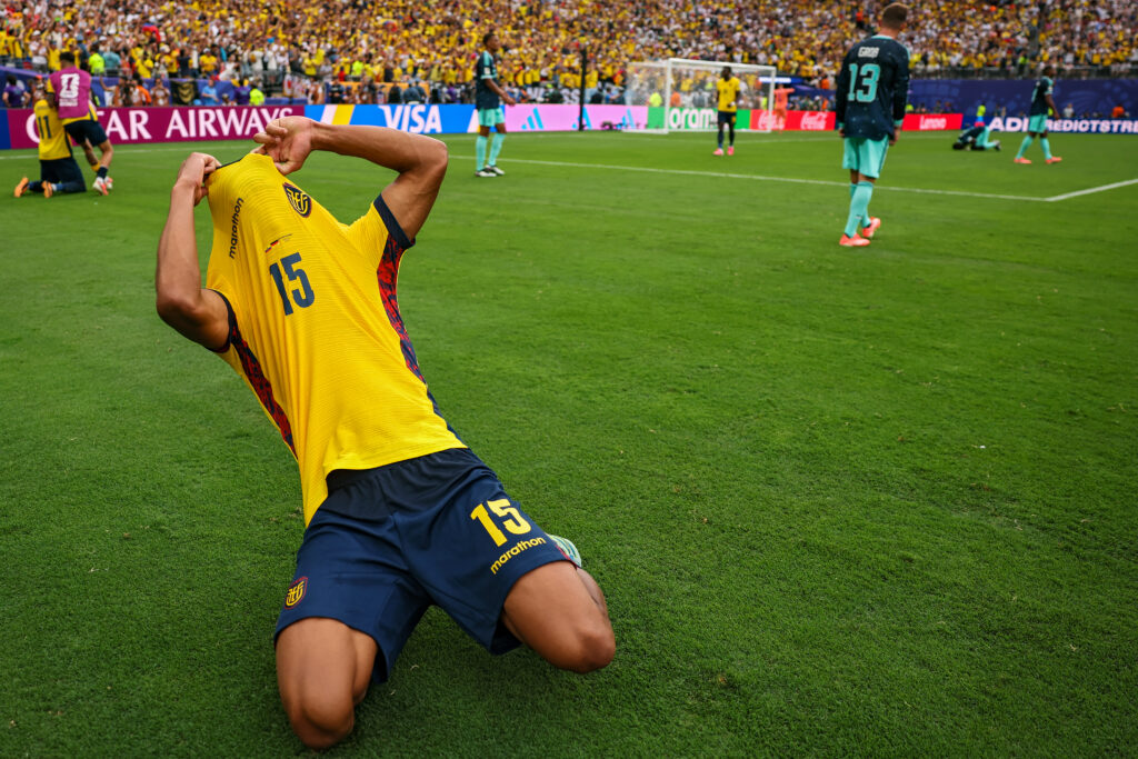 Soccer player in a yellow jersey #15 sliding on the grass during a match with a cheering crowd in the stands behind.