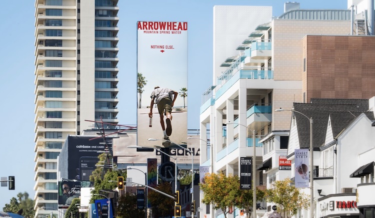 Urban street scene with tall advertising billboards; prominent Arrowhead Mountain Spring Water billboard shows a man diving into water with the words 'NOTHING ELSE' above.