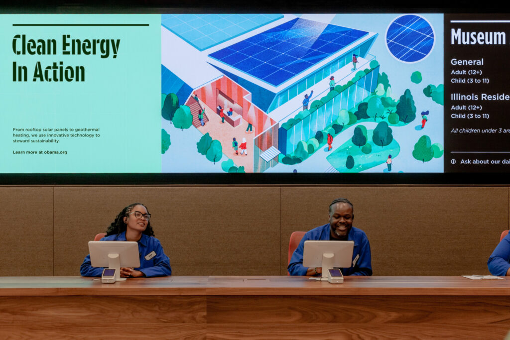 OPC_Lobby-detail©Manual | Muse by Clios Panel discussion at a podium with two people at a table, a large screen behind showing 'Clean Energy In Action' and a stylized building illustration.