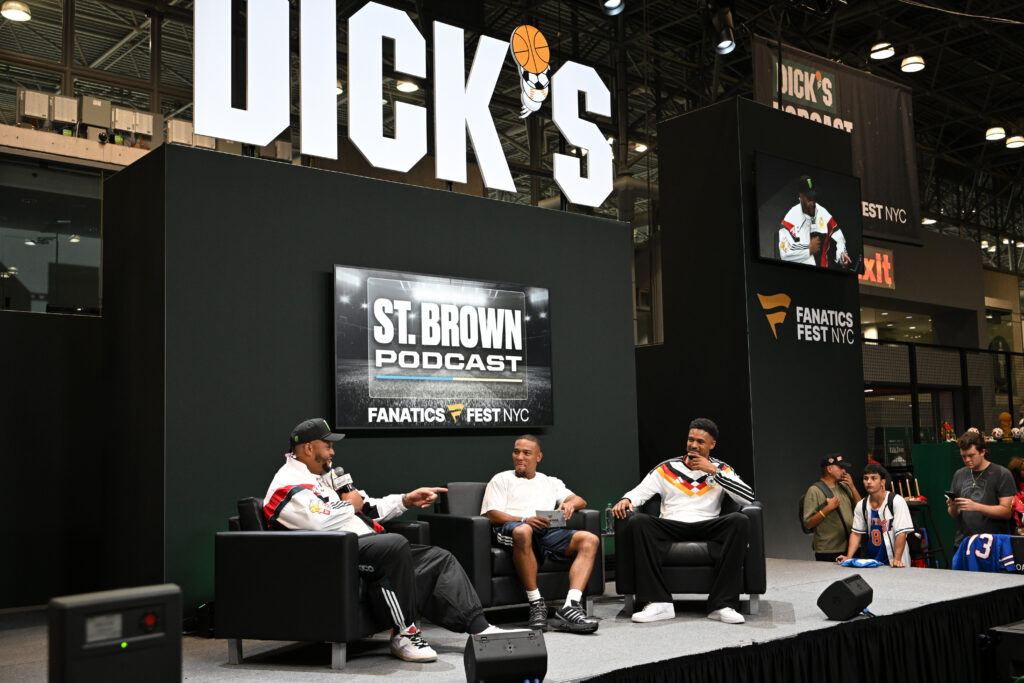Panel discussion on a stage at Fanatics Fest NYC, with large'DICK'S' sign and screens showing 'ST. BROWN PODCAST'