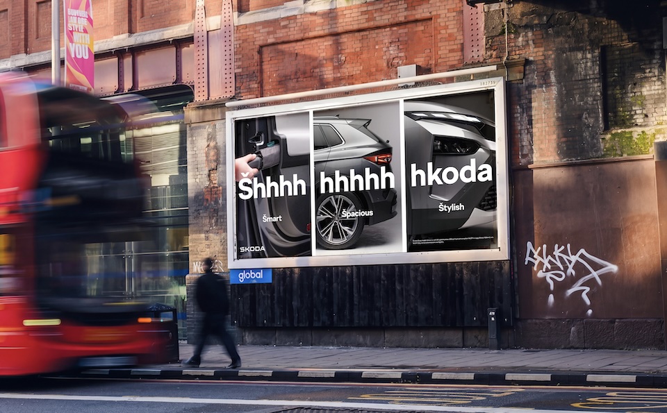 Street scene with a blurred red bus and a Skoda car advertisement displaying'Shhhh' and the words 'Smart', 'Spacious', 'Stylish'.