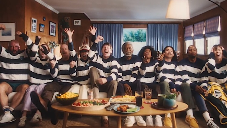Group of people wearing matching black-and-white striped sweaters sitting on a couch in a living room, arms raised in celebration around a coffee table with snacks.