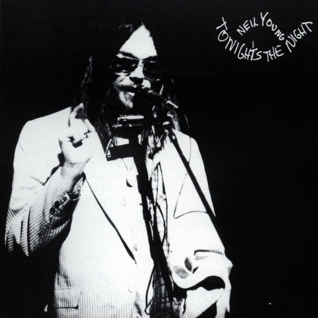 Black-and-white photo of Neil Young performing on stage, wearing a light suit and sunglasses, singing into a microphone; 'Tonight's the Night' appears in the top-right corner.