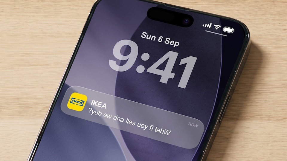 iPhone on a wooden surface showing 9:41 with a small IKEA notification banner labeled IKEA on the screen.