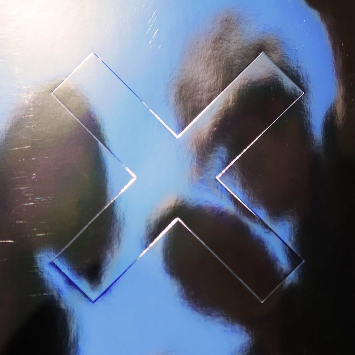 Close-up of a reflective blue-tinted metal surface with a large X-shaped cutout or indentation.