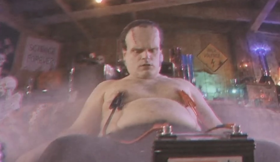 Frankenstein's monster, shirtless, strapped to electrical equipment in a smoky, cluttered lab.