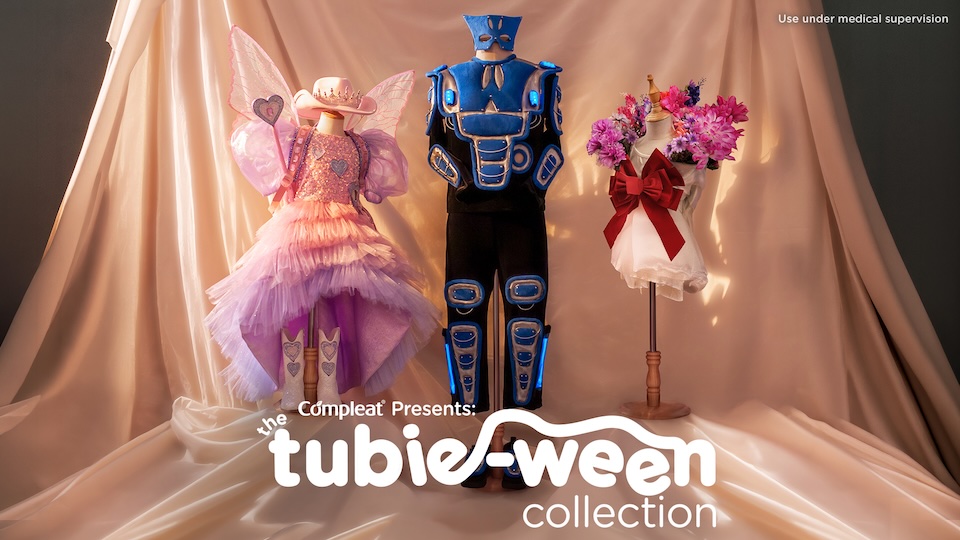 Three display mannequins in colorful costumes—a pink fairy dress, a blue armored suit, and a white dress with pink flowers—on a satin backdrop for the Tubie-Ween collection.